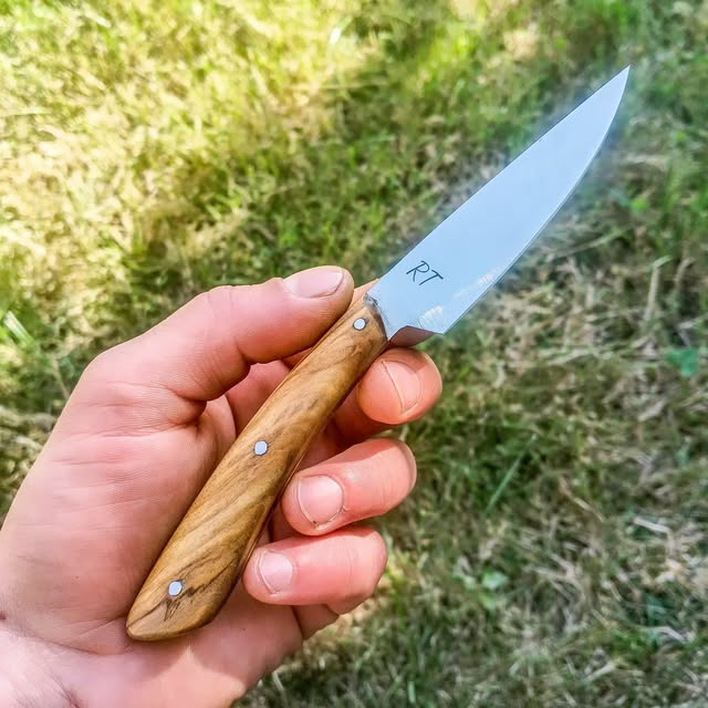 Couteau signé RT au manche en bois, présenté dans la main de l’artisan